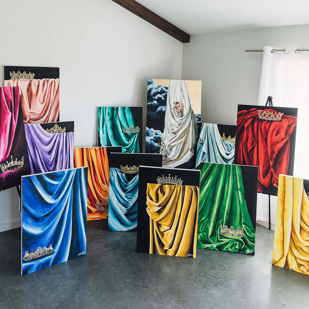 Rainbow collection art prints with colorful mantles and crowns, titled 'Garments of Praise: Mantled to Reign', displayed in a bright room.