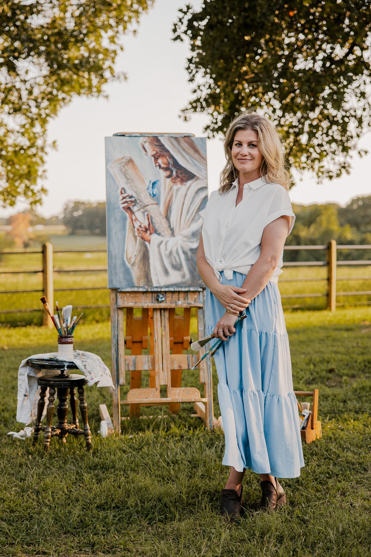 

Mindi standing beside her Jesus painting on an easel outdoors.