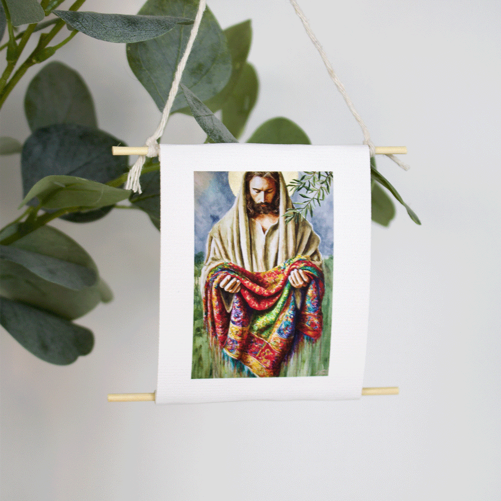 Mini collectible art of Jesus holding a multicolored coat, inspired by Joseph’s robe — Garment of Promise by Mindi Oaten, hanging with natural twine.