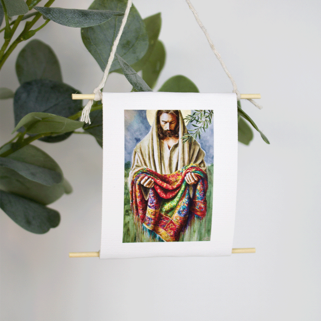 Mini collectible art of Jesus holding a multicolored coat, inspired by Joseph’s robe — Garment of Promise by Mindi Oaten, hanging with natural twine.