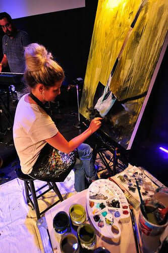 

Mindi painting a garden-spade artwork during a live gathering.