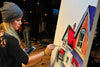

Mindi painting colorful houses at an easel during a live event.