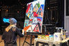 

Mindi painting colorful houses at an easel during a live event.