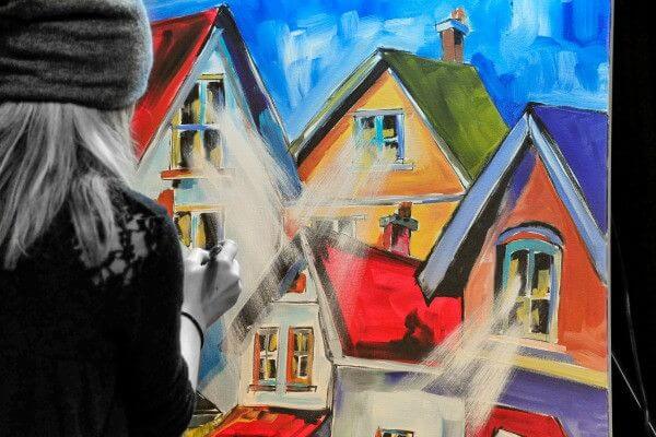 

Mindi painting colorful houses at an easel during a live event.