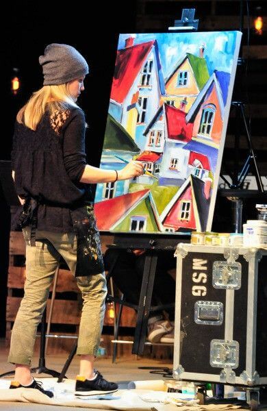 

Mindi painting colorful houses at an easel during a live event.