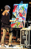 

Mindi painting colorful houses at an easel during a live event.
