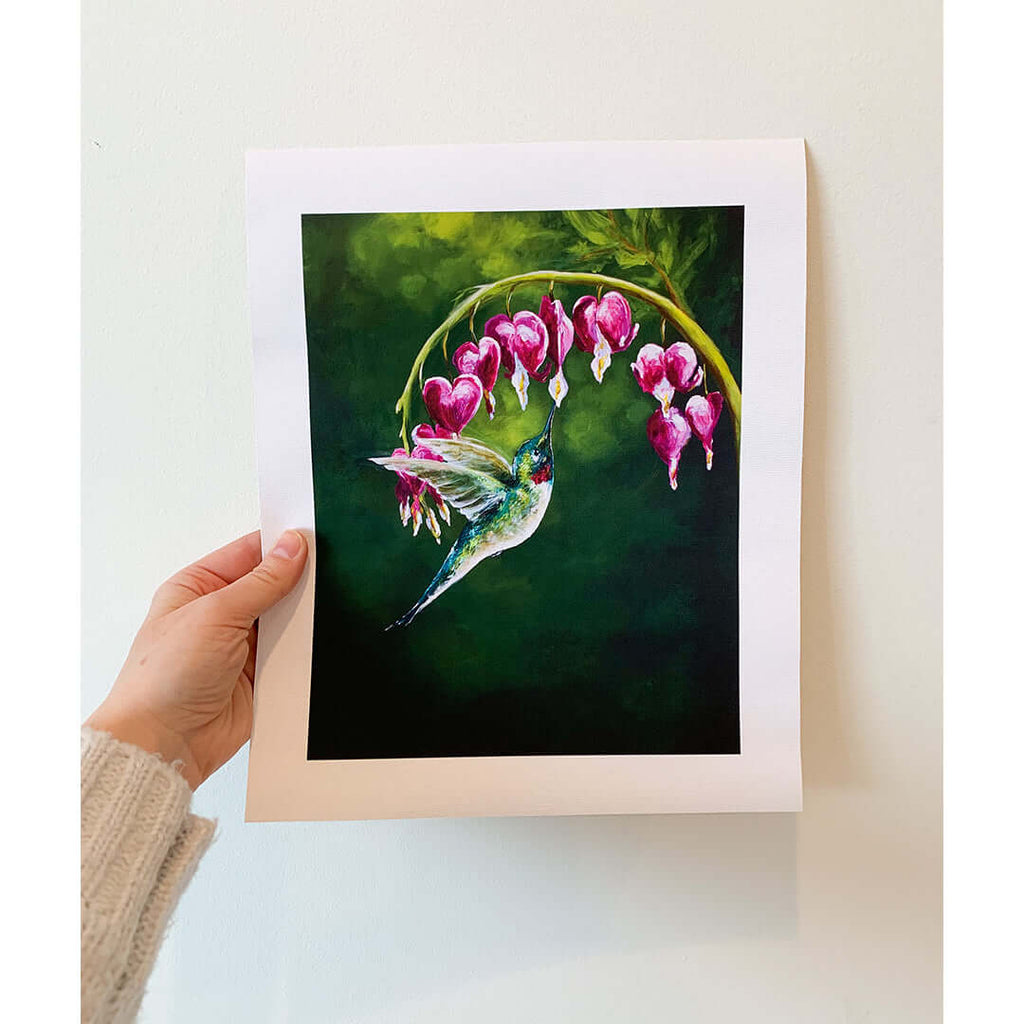 

A hand holding a print of the hummingbird and pink flower painting.